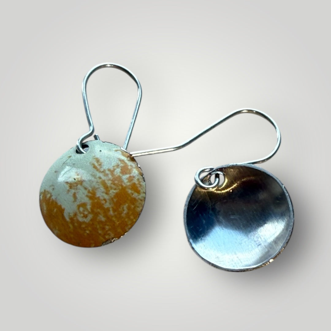 Pair of round earrings with glossy finish on a yellow brushed  background.